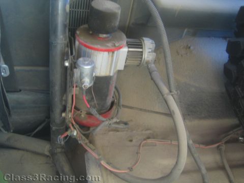 1990 Ford Bronco - close-up of an air filter canister, inline fuel filter and red wiring mounted against the dusty firewall of an off-road vehicle.
