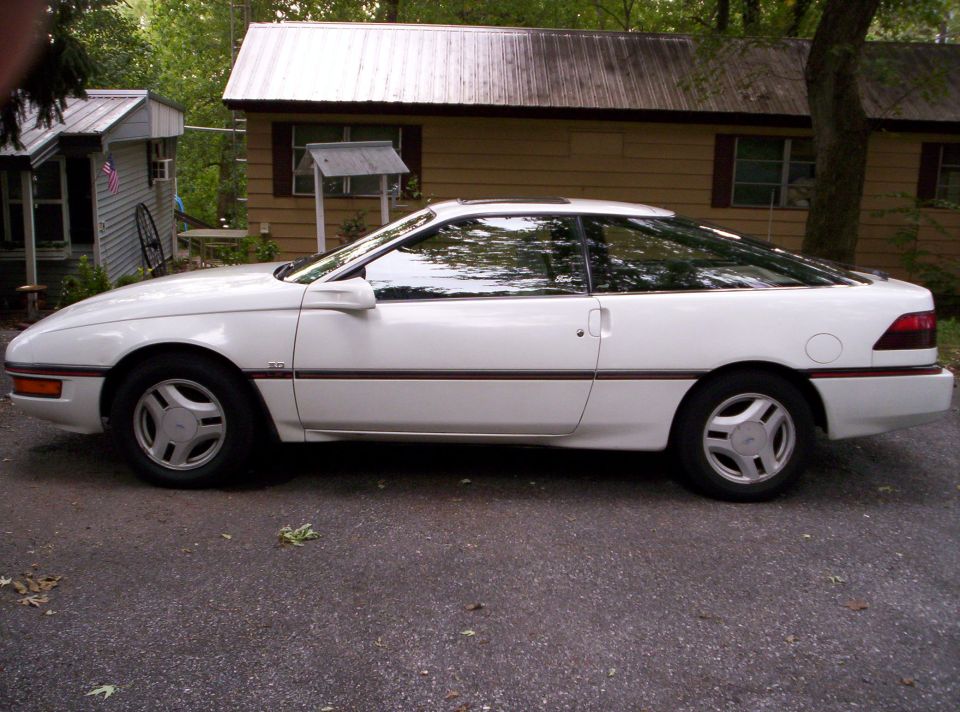 White Ford Probe coupe in side profile parked on gravel driveway near a house.