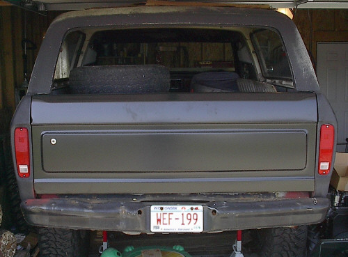 Rear tailgate of a gray Ford truck or Bronco with spare tire, Wisconsin plate WEF-199, in a garage