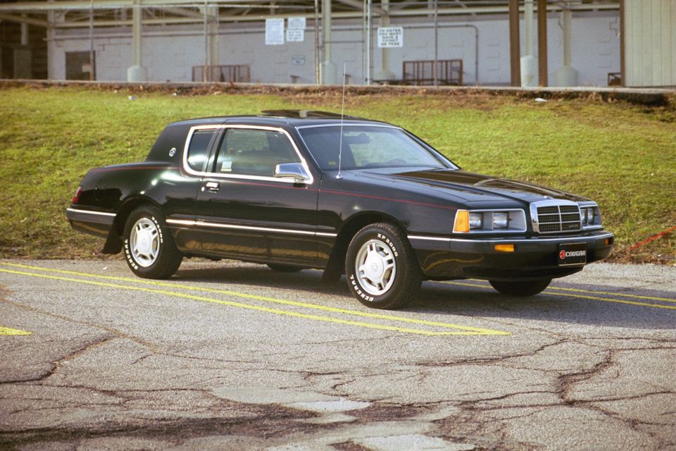 Black Mercury Cougar coupe with red pinstripe parked on cracked pavement, front three-quarter view.