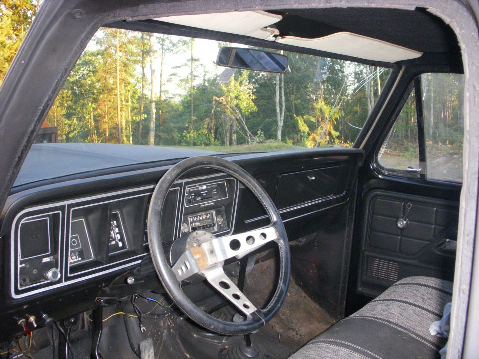 Interior view of a truck's dashboard and steering wheel, looking out the windshield at trees