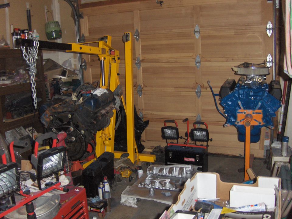 Garage engine swap with a used V8 on a hoist and a rebuilt blue Ford V8 on a stand