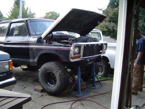 1979 Ford Bronco - Black Ford Bronco undergoing maintenance on jack stands, with a white truck visible in the background.