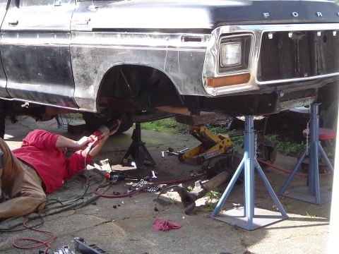 1979 Ford Bronco - Mechanic works on the front suspension of a 1979 Ford Bronco, which is raised on jack stands.