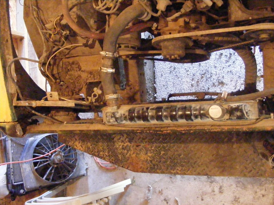 Engine bay showing radiator, fan, hoses, and belts. Some rust and dirt are visible