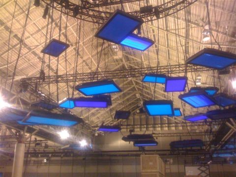 1994 Ford Bronco - An array of blue illuminated panels hang from the ceiling structure of a large indoor venue.