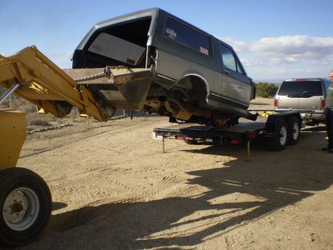 1996 Ford Bronco - A gray SUV is being lifted onto a trailer by a yellow loader, with another SUV visible in the background.