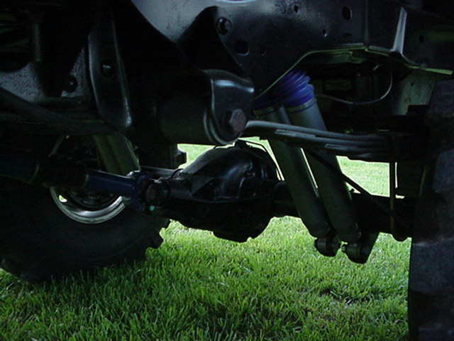 Underside of lifted truck showing solid axle, differential, leaf springs, dual shocks and blue steering stabilizer