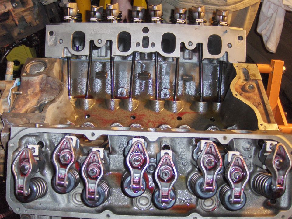Partially assembled V8 engine showing open lifter valley, pushrods, and rocker arms with red assembly lube