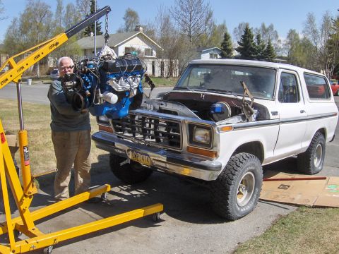 1978 Ford Bronco - A man uses an engine hoist to remove the engine from a white 1978 Ford Bronco.