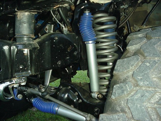 Front coil-spring suspension with blue-booted shock and steering stabilizer on a solid axle