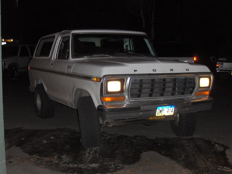 White Ford Bronco at night with headlights on, front three-quarter view in snow