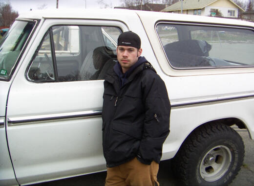 Person in black jacket leaning against the side of a white full-size Ford Bronco