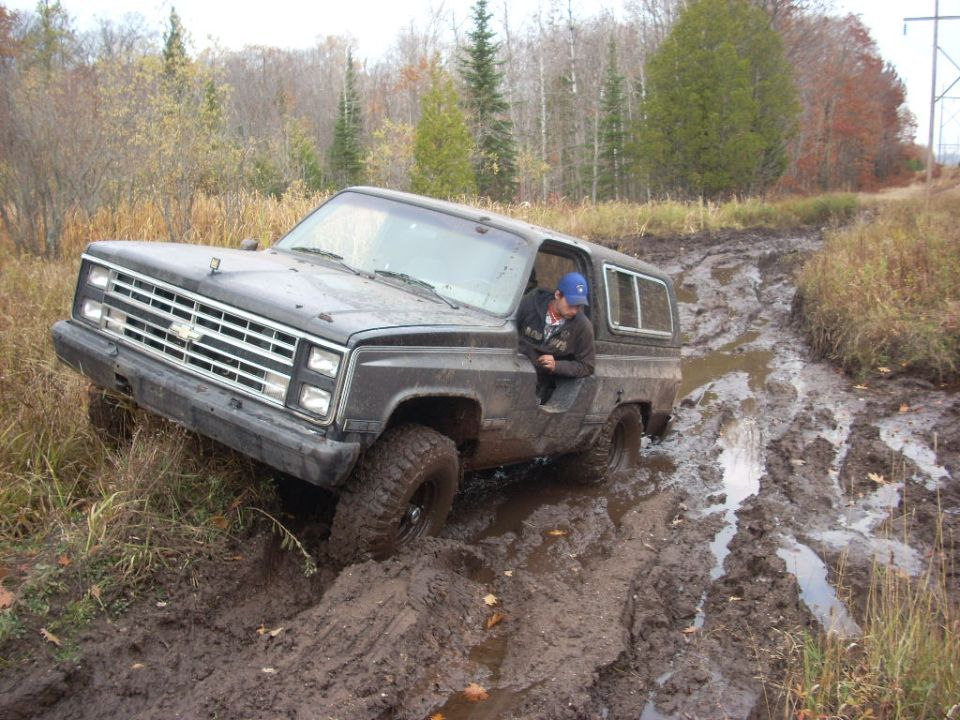 Dark gray 1988 Chevrolet Blazer stuck in mud, driver's side front tire deep in mire
