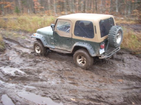 1988 Chevrolet Blazer - Jeep Wrangler navigating a muddy trail, with one wheel deep in the mire.
