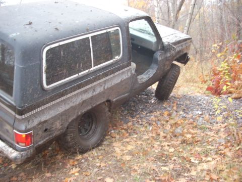 1988 Chevrolet Blazer - A dark SUV with a camper shell is tilted on a gravel path with the driver's door open.
