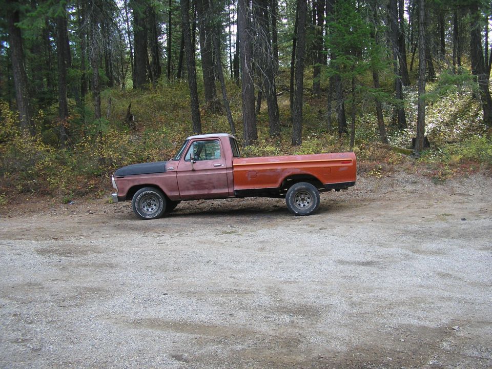 Red and orange 1977 Ford F-150 pickup truck parked on a gravel road with trees in the background