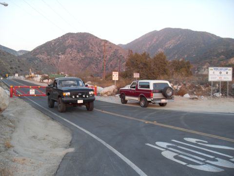1990 Ford Bronco - Two trucks, a Bronco and an F-150, are stopped on a road with mountains in the background.