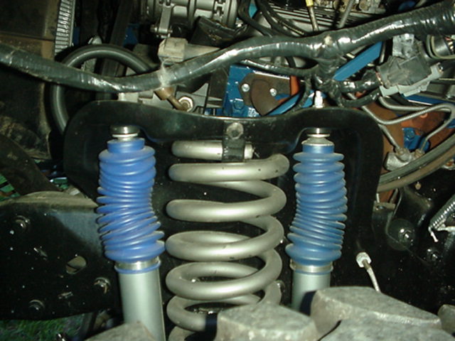 Coil spring and two shocks with blue dust boots in a vehicle suspension.