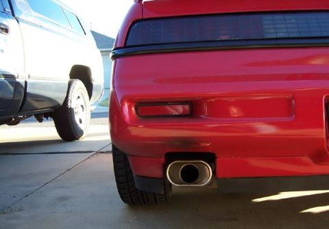 1988 Pontiac Fiero - Rear view of a red 1988 Pontiac Fiero showing its bumper and exhaust pipe, with a white SUV to the left.