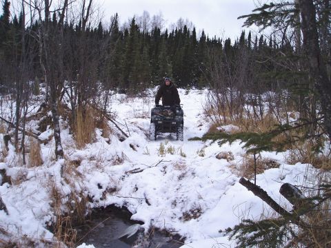 2000 Ford E350 - Person rides an ATV through a snowy, wooded landscape.