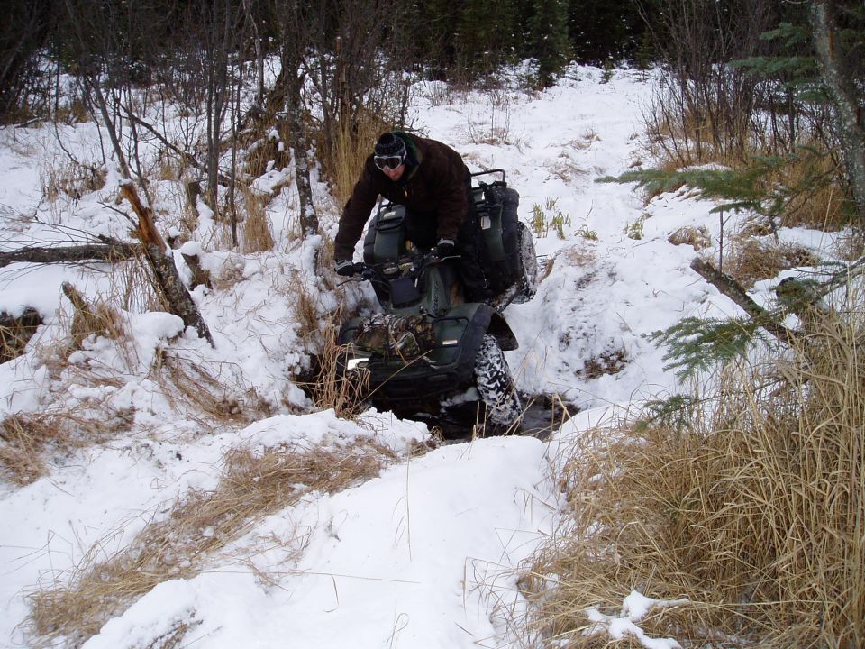 Guy riding an ATV through a snowy ditch with trees around