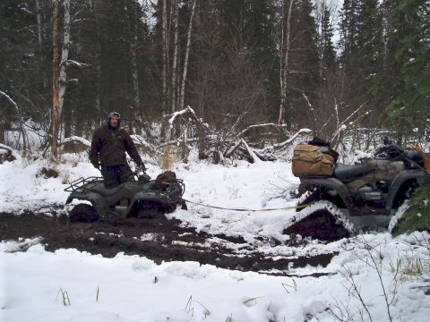 2000 Ford E350 - Two ATVs are stuck in the mud and snow in a wooded area. One ATV is being pulled by a tow strap.