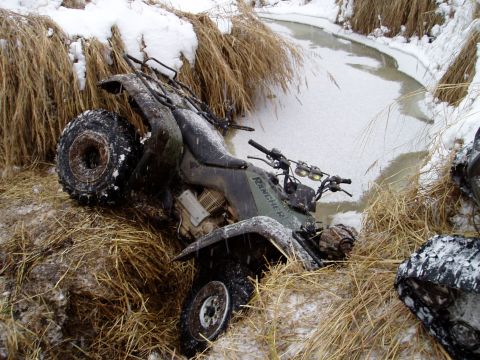 2000 Ford E350 - An ATV is partially submerged in a frozen stream surrounded by snow and dry grass.