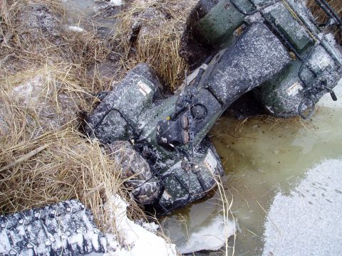 2000 Ford E350 - An ATV is stuck in a muddy, watery ditch, partially covered in snow and surrounded by dry grass.
