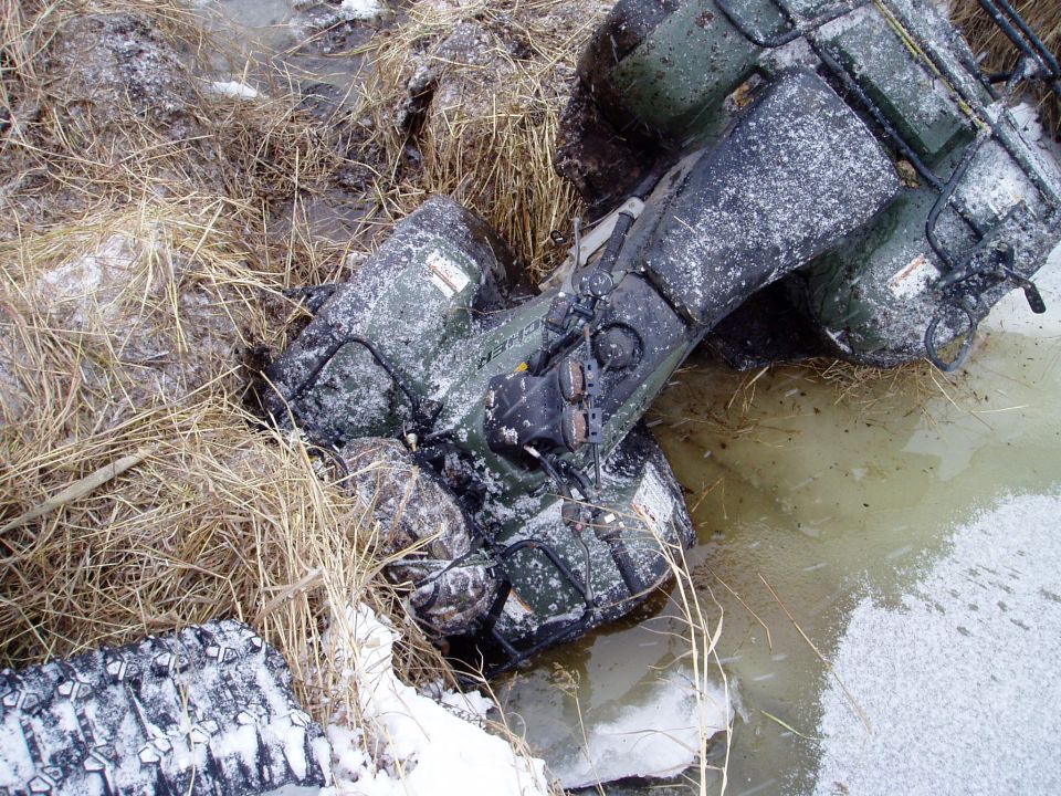 Green ATV stuck in muddy water with snow and dry grass