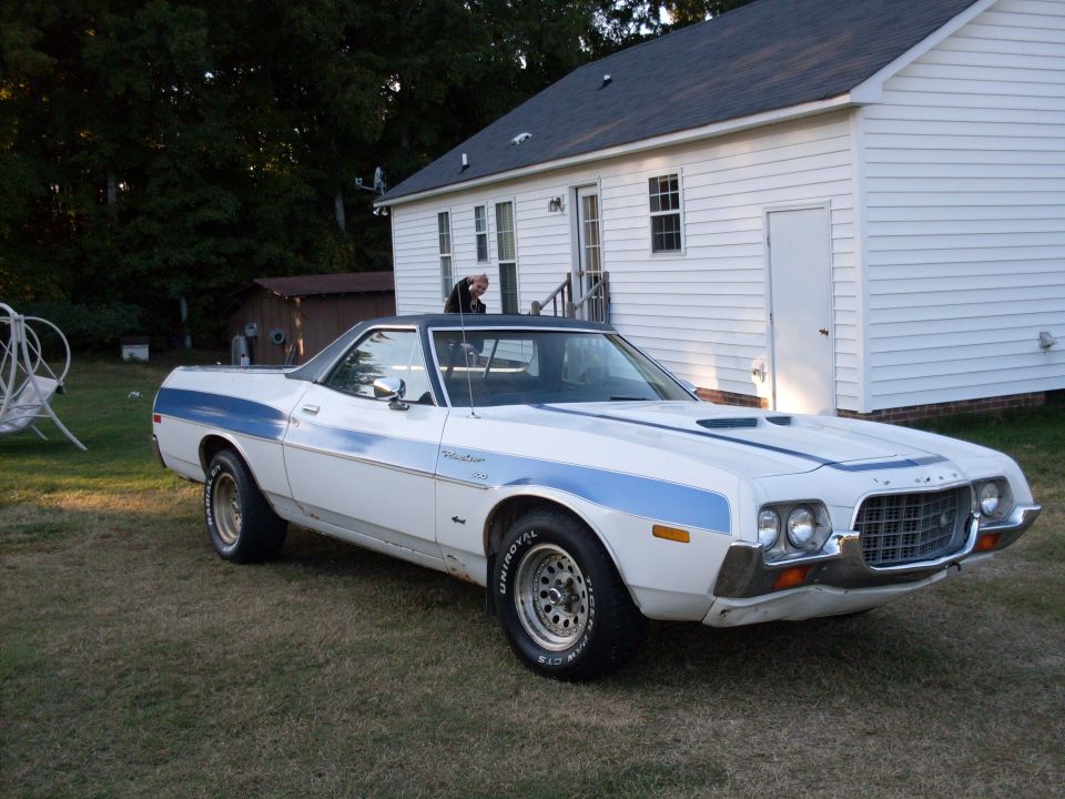 White 1972 Ford Ranchero with blue stripe parked on grass by a house.