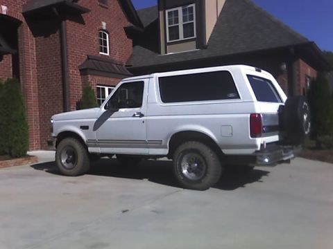 1996 Ford Bronco - This white Ford Bronco is parked in a driveway next to a large brick house.
