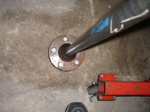 1988 Ford Bronco - A driveshaft flange and part of a driveshaft are shown on a concrete floor with a jack stand nearby.