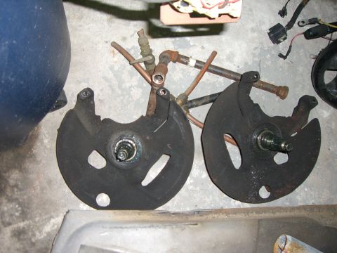 1988 Ford Bronco - Two brake dust shields and associated plumbing components are laid out on a concrete floor.