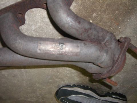 1988 Ford Bronco - Ford exhaust manifold part with visible logo and text. A shoe is in the foreground.