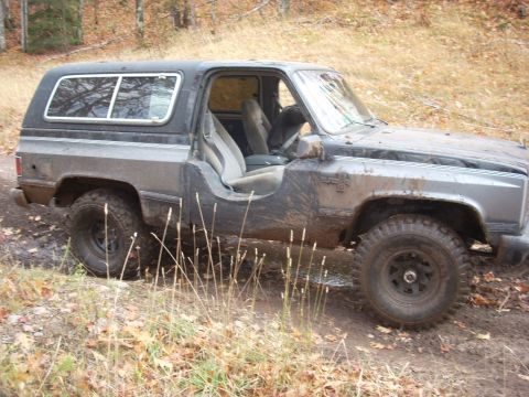 1988 Chevrolet Blazer - This SUV is covered in mud and appears to be off-roading in a wooded area.