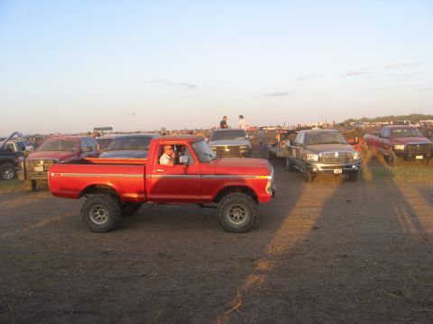 1979 Ford Bronco - A red pickup truck with a lifted suspension is parked outdoors among other vehicles.