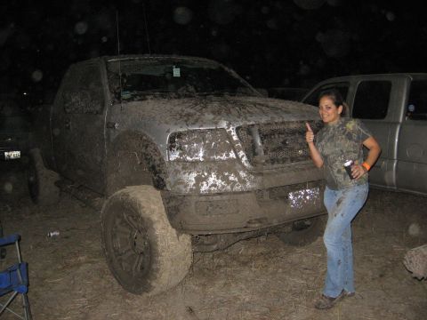 1979 Ford Bronco - A woman poses next to a heavily mud-covered pickup truck at night.