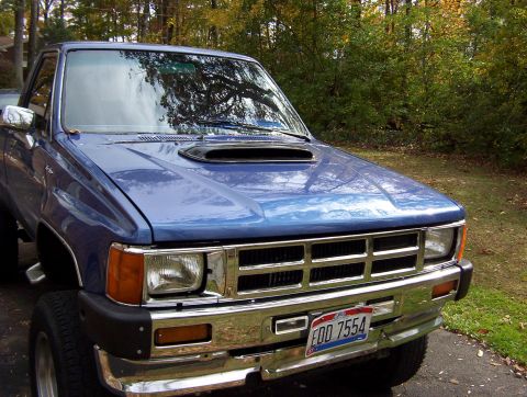1986 Toyota Hilux - A blue pickup truck with a prominent hood scoop is parked outdoors, showing its front grille and bumper.