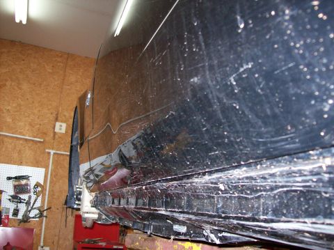 2007 Ford Mustang - Side view of a black car showing extensive damage to the lower body panels while elevated on a hoist.