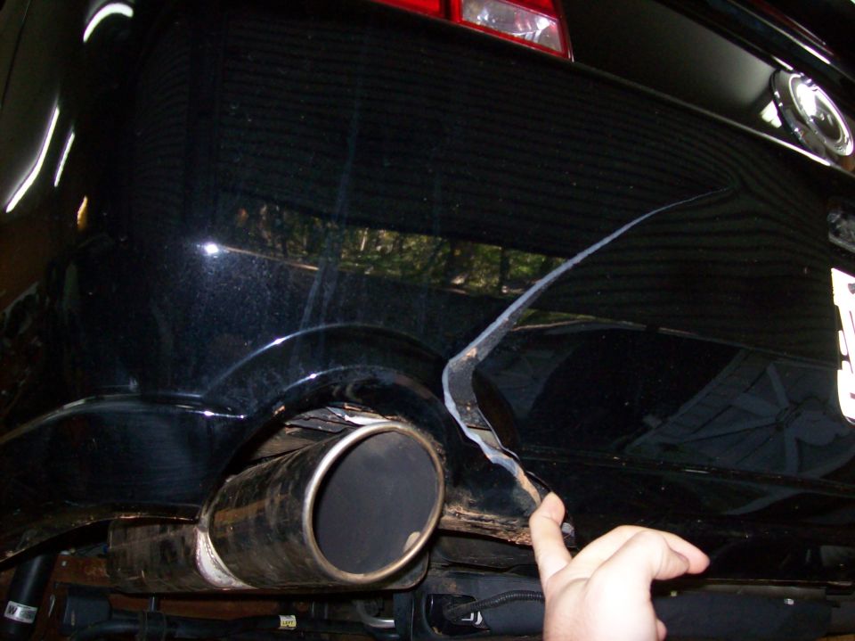 2007 Ford Mustang rear bumper with a large crack and exposed metal, showing exhaust pipe