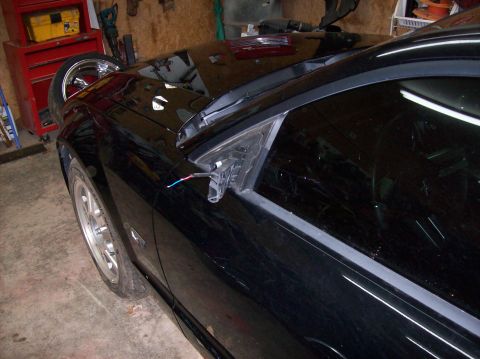2007 Ford Mustang - A black car's side mirror is detached, revealing wires, inside a workshop.