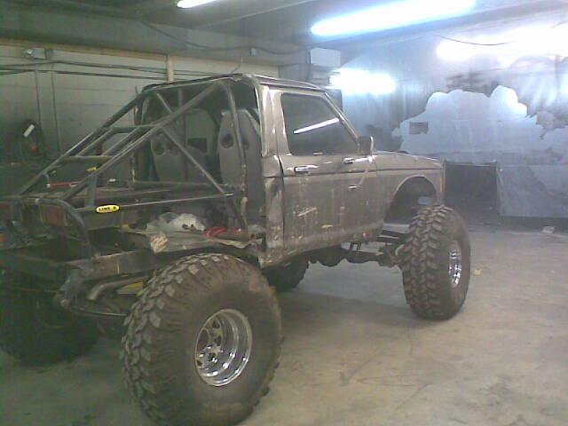 Custom off-road SUV with a roll cage, large tires, and lifted suspension, parked indoors