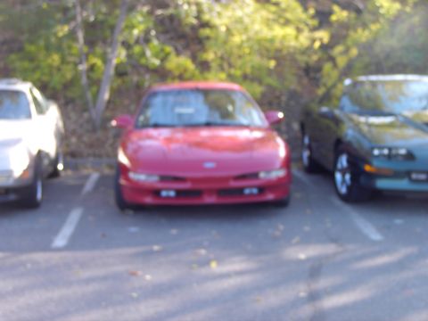 1991 Ford Probe - Three cars parked in a lot, with a red 1991 Ford Probe in the center.
