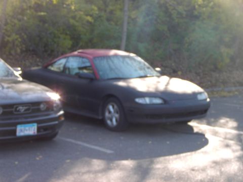 1991 Ford Probe - A dark coupe with a red roof is parked next to a Ford Mustang in a parking lot.