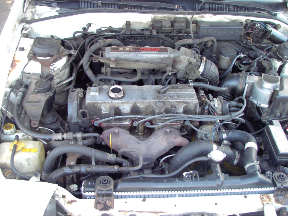 Engine bay of a 1991 Ford Probe, showing the 2.2L turbo engine with visible hoses, wiring, and radiator
