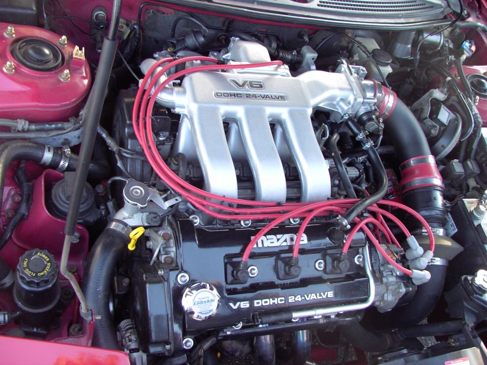 Engine bay shot showing a V6 DOHC 24-valve Mazda engine with red spark plug wires