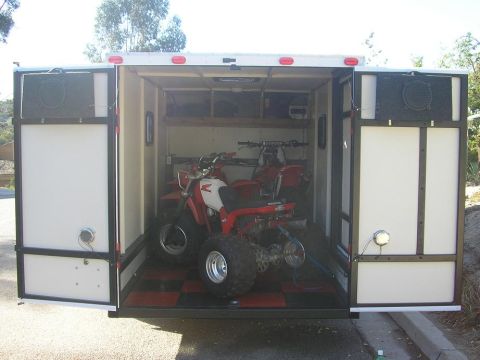1900 Honda Big Red - Two ATVs are parked inside an open trailer, with one in the foreground and another behind it.