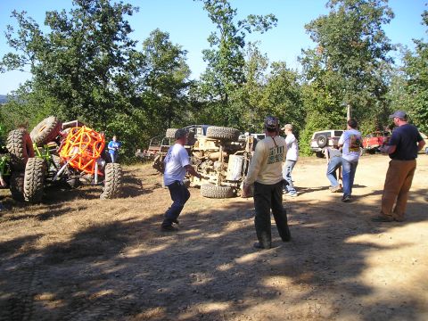 1989 Ford Bronco - Several off-road vehicles are present in a dirt lot, with one vehicle overturned on its side.
