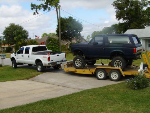 1995 Ford Bronco - A lifted Ford Bronco is transported on a trailer pulled by a white Ford F-250 pickup truck.